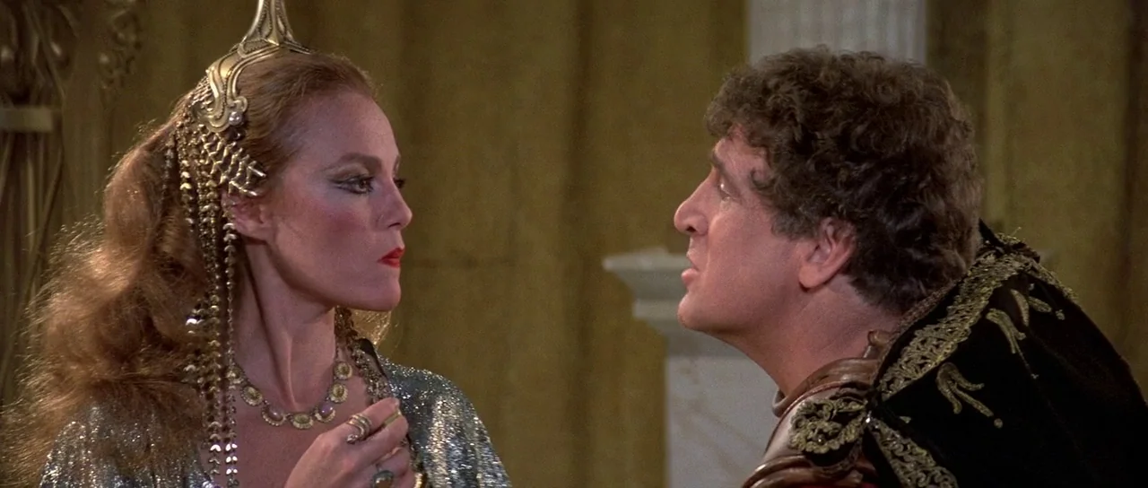 History of the World: Part 1 (1981) movie still: medium — A stone-walled interior space features columns and draped fabrics in a golden-toned…
