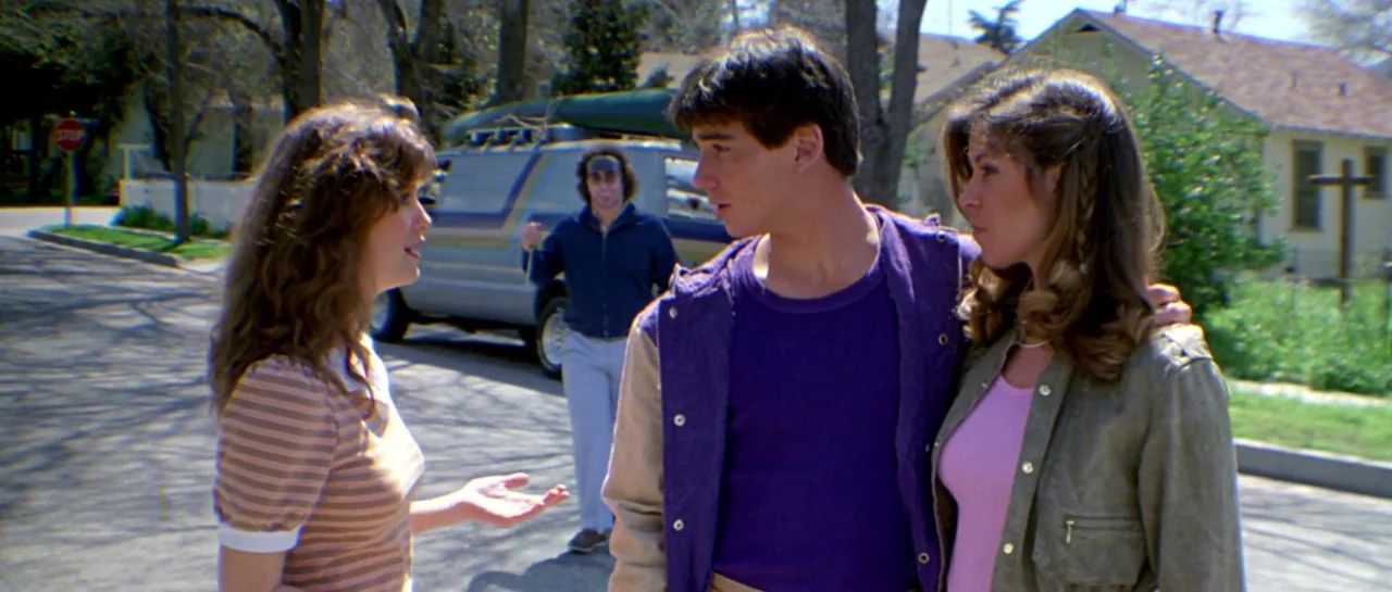 Friday the 13th Part III (1982) movie still: medium — A suburban street intersection with trees and houses in the background under daylight. Three…