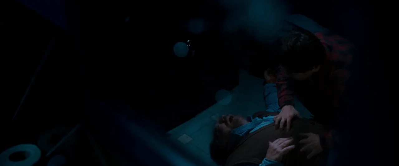 The Autopsy of Jane Doe (2016) movie still: medium — A dimly lit tiled floor in a room with blue ambient light. A person kneels over an older man…