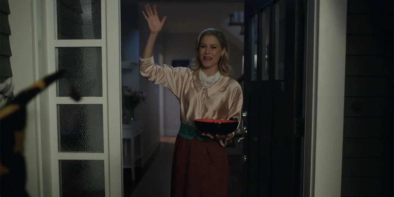 Totally Killer (2023) movie still: medium — A residential entryway at night shows a woman standing in an open doorway. She wears a blouse and skirt…