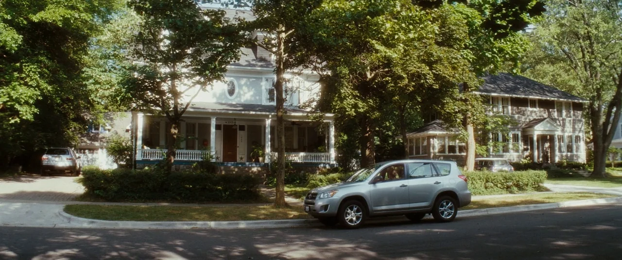 Scream 4 (2011) movie still: establishing — A quiet suburban street features two large, multi-story houses surrounded by mature green trees. A…