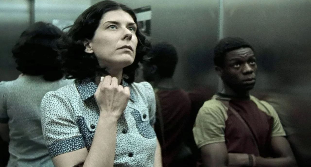 City of God (2002) movie still: medium — An elevator interior with metallic walls reflects the people inside. A woman in a patterned blouse stands…