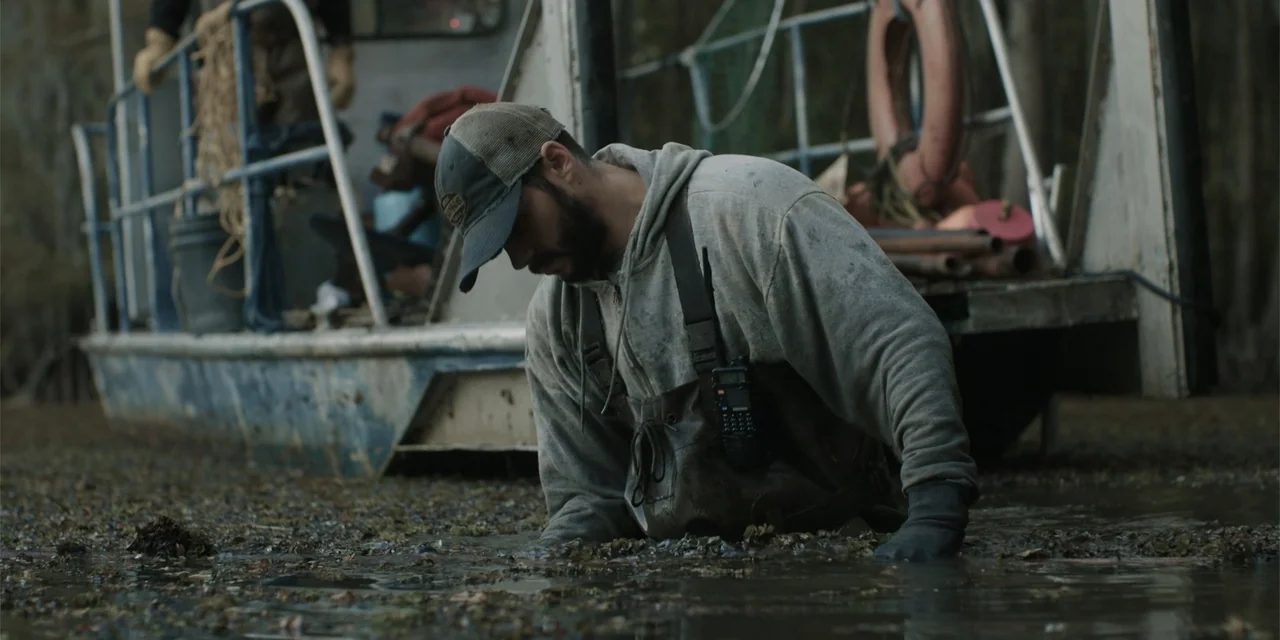 Caddo Lake (2024) movie still: medium — A murky swamp environment features a weathered metal flat-bottom boat partially visible behind. A man…