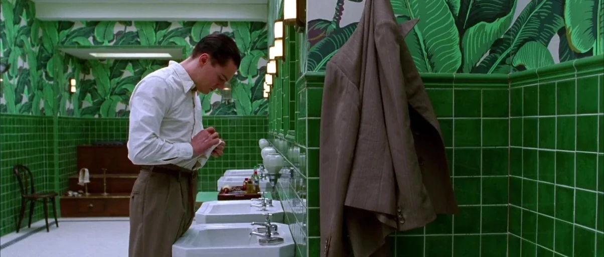 The Aviator (2004) movie still: medium — A restroom features vibrant green square tiles and distinctive banana leaf patterned wallpaper above. A man…