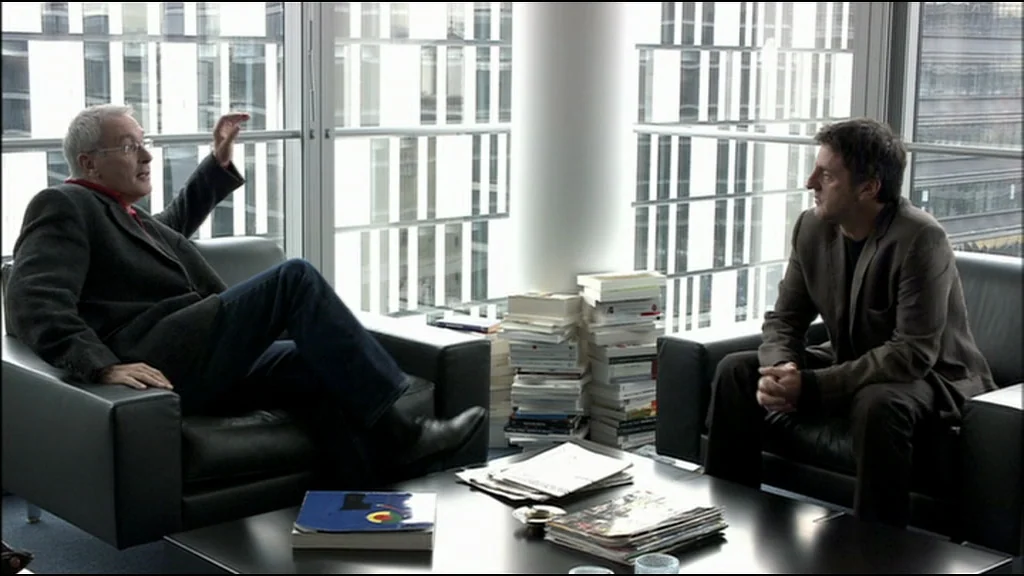 Caché (Hidden) (2005) movie still: medium — A modern office features floor-to-ceiling windows overlooking a glass-paneled skyscraper exterior. Two…