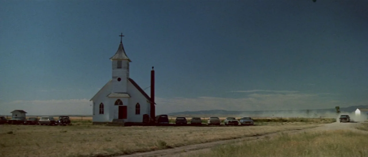 Thunderbolt & Lightfoot (1974) movie still: establishing — A small white rural church stands alone on a dry, grassy expanse. A single dark car kicks…