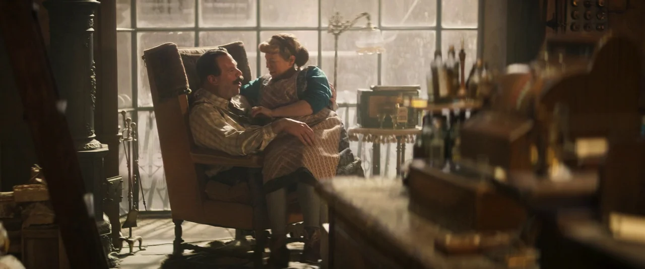 Wonka (2023) movie still: medium — A dimly lit room filled with vintage store fixtures and glass window panes. A middle-aged man sits in an armchair…