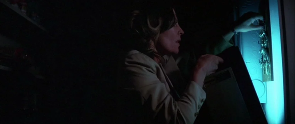 Demon Seed (1977) movie still: medium — A dark utility space with a wall-mounted panel containing a key rack. A woman stands in the shadows,…