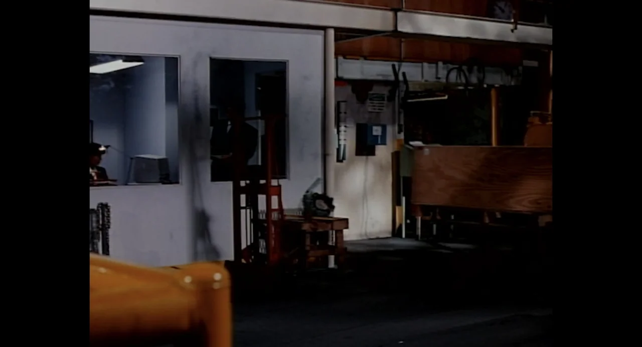American Yakuza (1993) movie still: wide — A spacious warehouse interior features a partitioned white office structure with large rectangular…