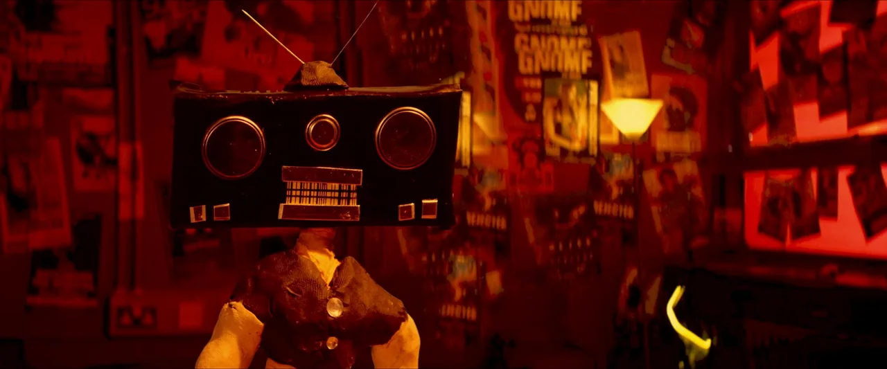 Kneecap (2024) movie still: medium — A dark space decorated with many posters and illuminated by an intense red light. A figure with a television…