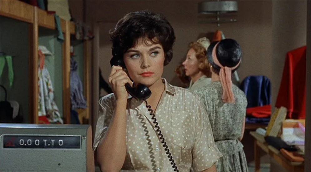 Kid Galahad (1962) movie still: medium — A dressing room area with wooden clothing racks and shelves holding folded garments. A woman stands in the…