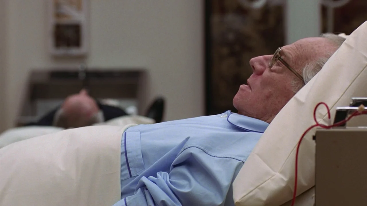 Being There (1979) movie still: medium — A sterile medical environment features multiple beds separated by a divider in the background. An elderly…