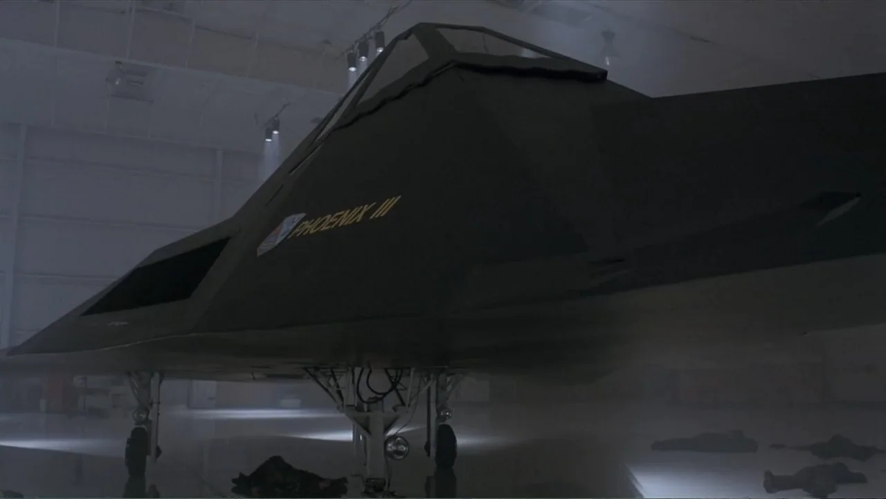 Crisis Point (2012) movie still: medium — A dark stealth aircraft sits in a sparse, misty, and dimly lit hangar. Several figures lie motionless on…