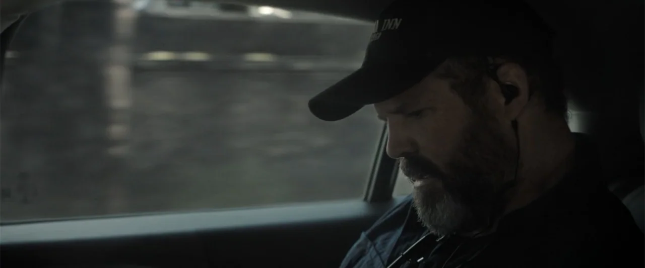 The Equalizer 3 (2023) movie still: closeup — A dark interior of a moving car with a window visible on the left. A middle-aged man with a dark beard…