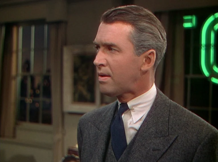 Rope (1948) movie still: medium — An interior space features walls painted in muted tones with a dark window backdrop. A man in a tailored suit…