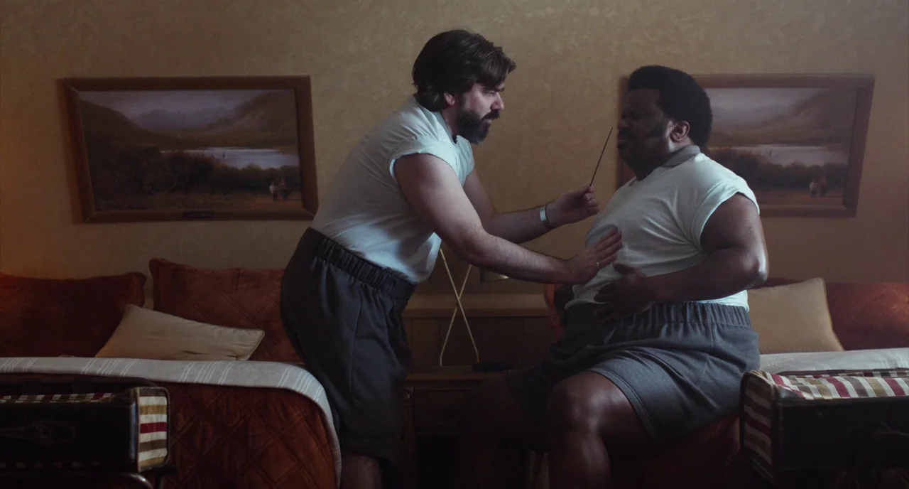 An Evening With Beverly Luff Linn (2018) movie still: medium — A motel room with framed landscape prints on beige textured wallpaper above two beds.…