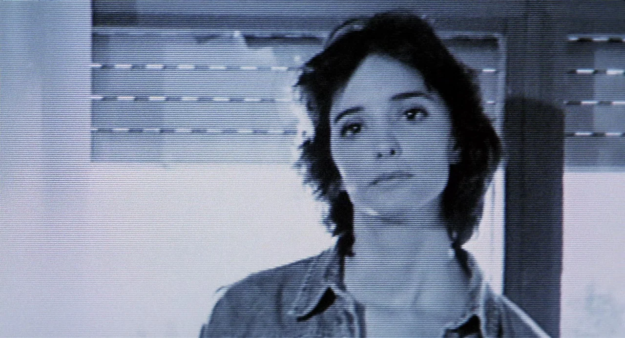 Thesis (1996) movie still: closeup — An interior space with horizontal blinds visible in the background through the scan lines. A woman with dark…