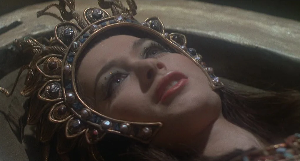Blood From The Mummy’s Tomb (1971) movie still: closeup — A woman wears an elaborate, jewel-encrusted gold headpiece while lying within a stone…