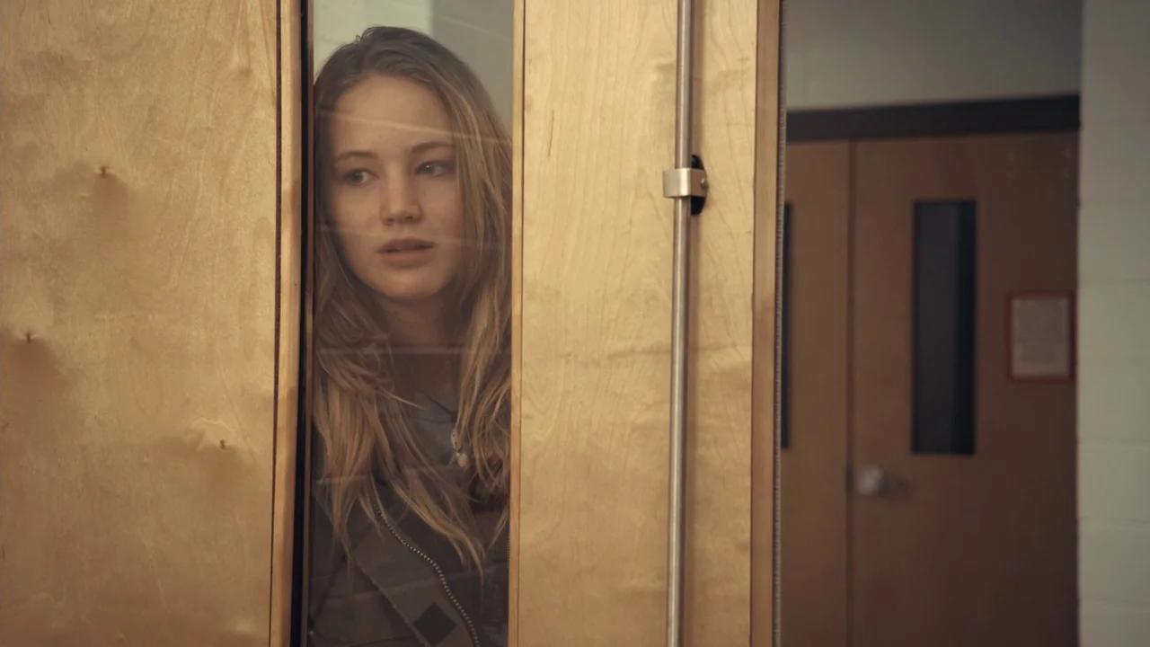 Winter’s Bone (2010) movie still: medium — A view through a wooden door window into a school hallway. A young woman looks through the glass gap at…