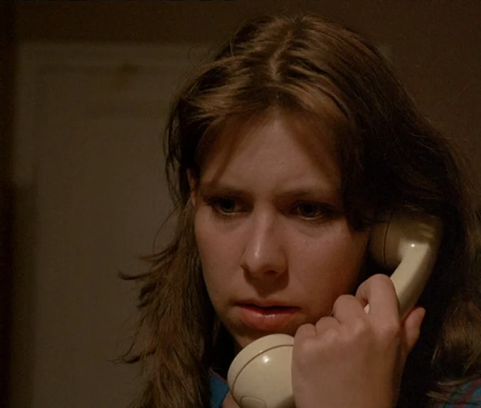 Crime & Punishment (1983) movie still: closeup — A dimly lit indoor space with neutral-colored walls. A young woman holds a beige telephone handset…