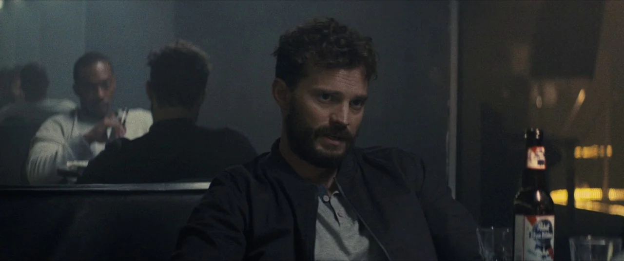 Synchronic (2019) movie still: medium — A dimly lit diner booth at night with soft ambient shadows. A man with a dark beard sits at a table near a…
