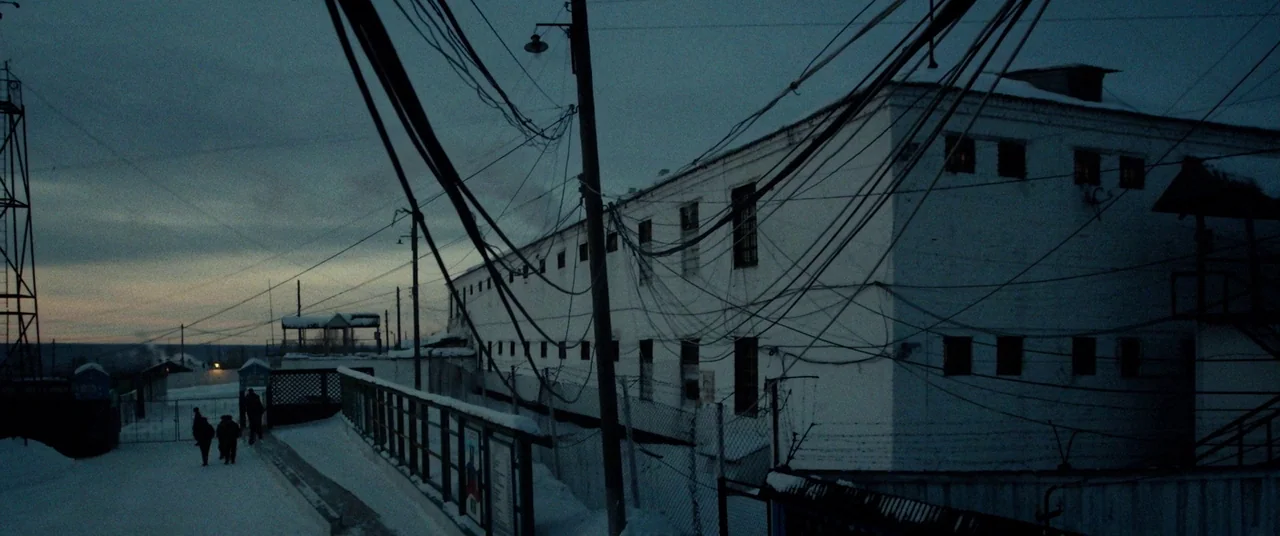 Triple 9 (2016) movie still: establishing — A long, white, two-story building stands in a snow-covered landscape during early dawn. Numerous utility…