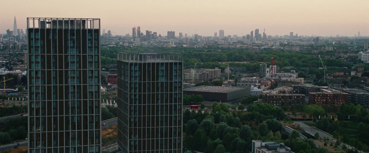 All Of Us Strangers (2023) movie still: establishing — A wide aerial view shows tall modern apartment towers in the foreground. The background…
