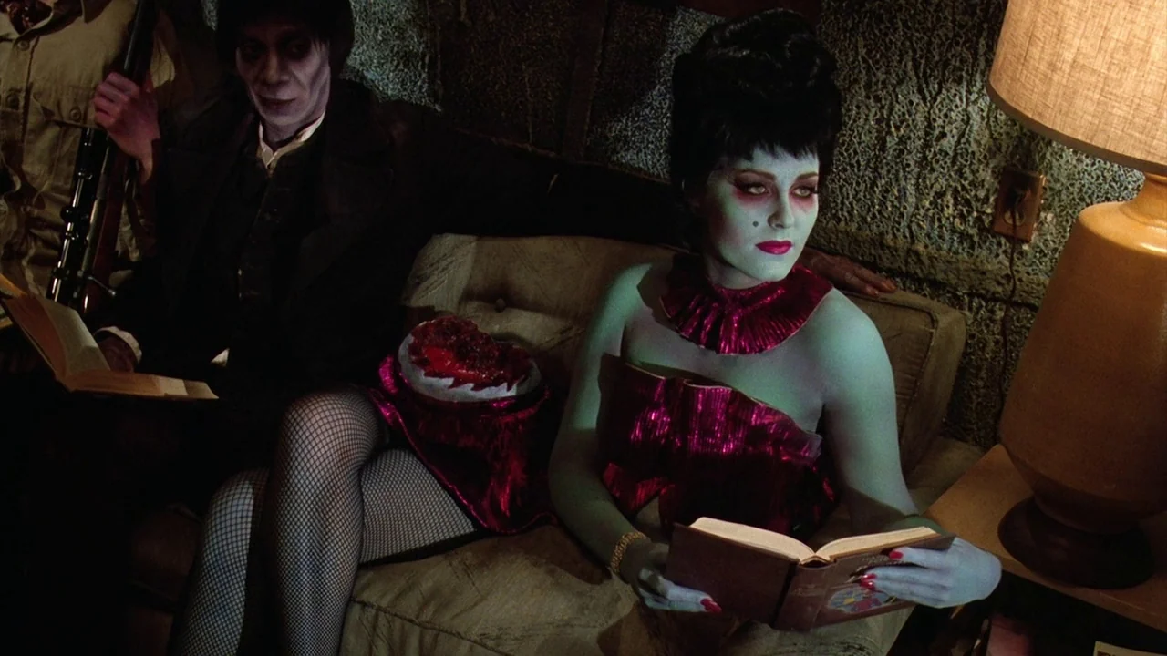 Beetlejuice (1988) movie still: medium — A dimly lit room features a worn sofa against a textured wall surface. A pale-skinned woman and a…