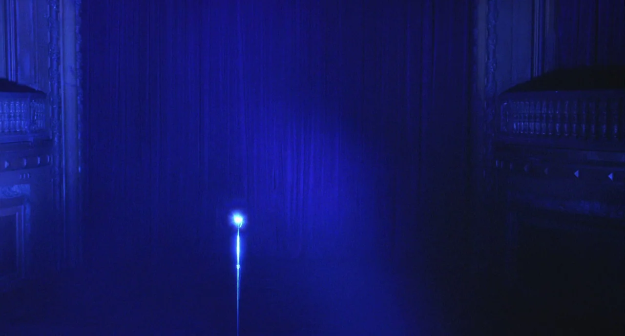 Mulholland Drive (2001) movie still: establishing — Dark blue velvet curtains hang behind a lone glowing pole on a dark stage. The area is dimly lit…