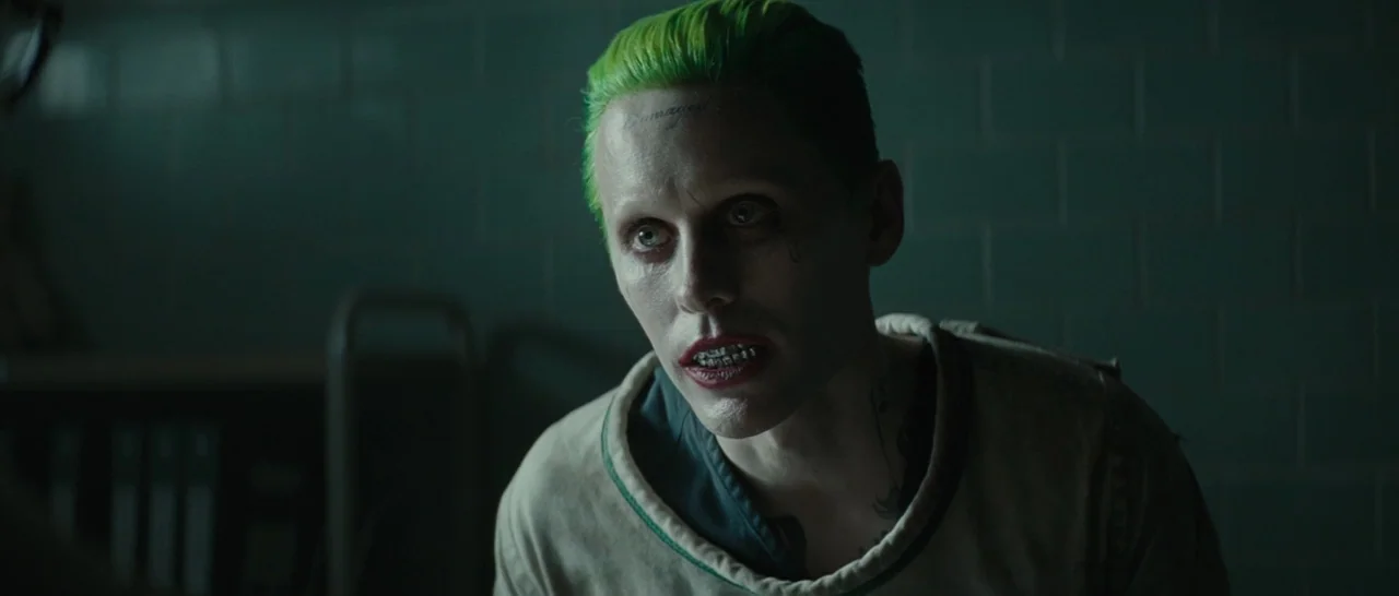Suicide Squad (2016) movie still: medium — A dimly lit room with muted green-tinted tiled walls appears cold and sterile. A pale man with green hair…