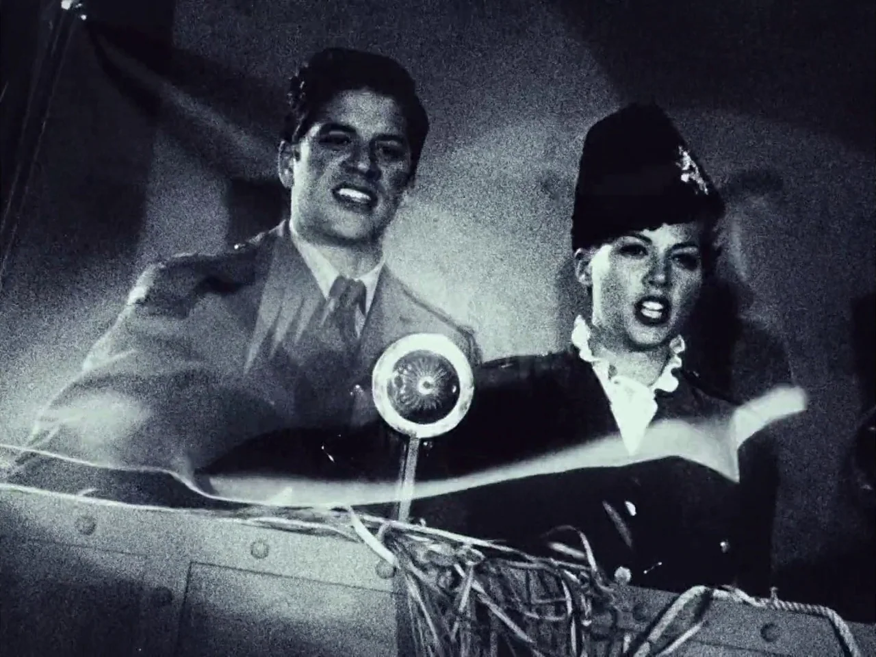 The Twentieth Century (2019) movie still: medium — A dimly lit stage with a silver vintage microphone centered between two performers. A man and a…