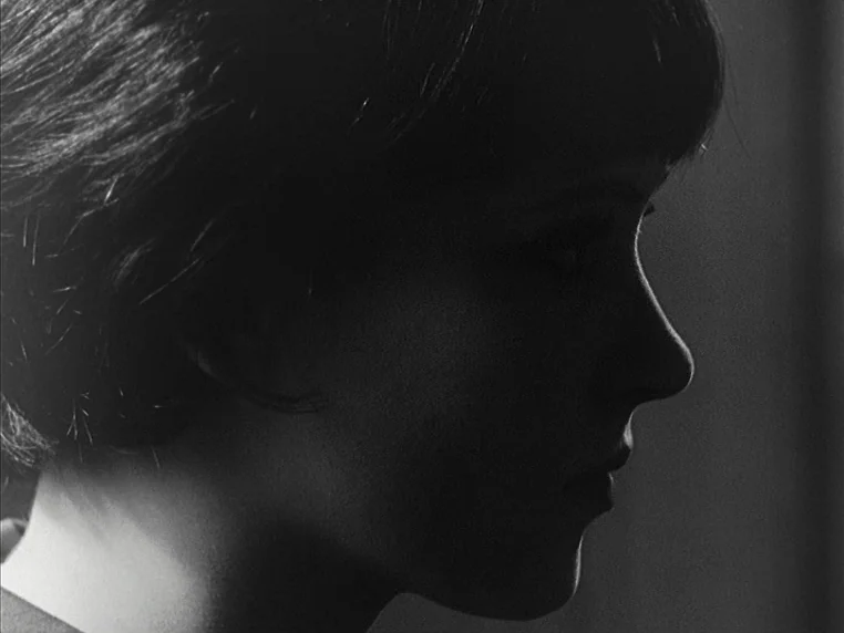 Vivre Sa Vie (1962) movie still: closeup — A close-up of a young woman's face seen in silhouette against a dark background. She is turned to the…