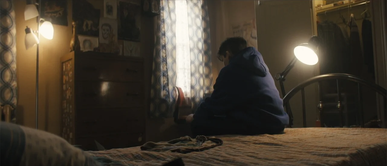 All Fun and Games (2023) movie still: medium — A cluttered bedroom with patterned curtains, a wooden dresser, and several wall posters. A teenager…