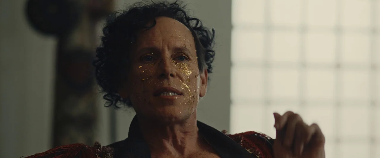 We Are Zombies (2023) movie still: closeup — An interior space features a person with gold leaf applied to their skin. The individual wears an…
