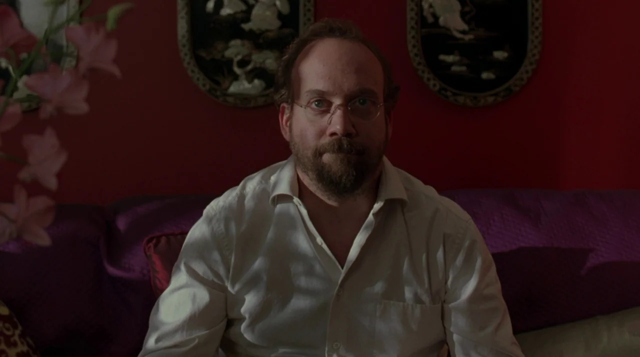 Lady in the Water (2006) movie still: medium — An interior space features red walls decorated with two black oval-framed art pieces. A man wearing a…