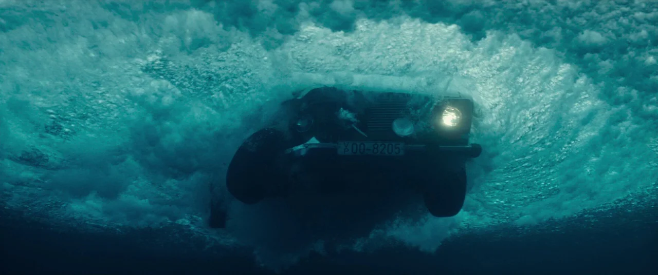 Atomic Blonde (2017) movie still: medium — A dark vehicle plunges into deep, turbulent water creating a large bubble field. One headlight remains…