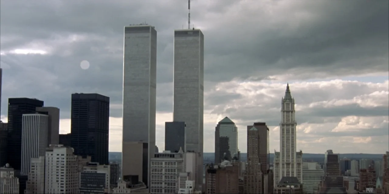 A Radical Life (2022) movie still: wide — A dense city skyline dominated by the twin towers under a cloudy sky. The architecture of Manhattan…