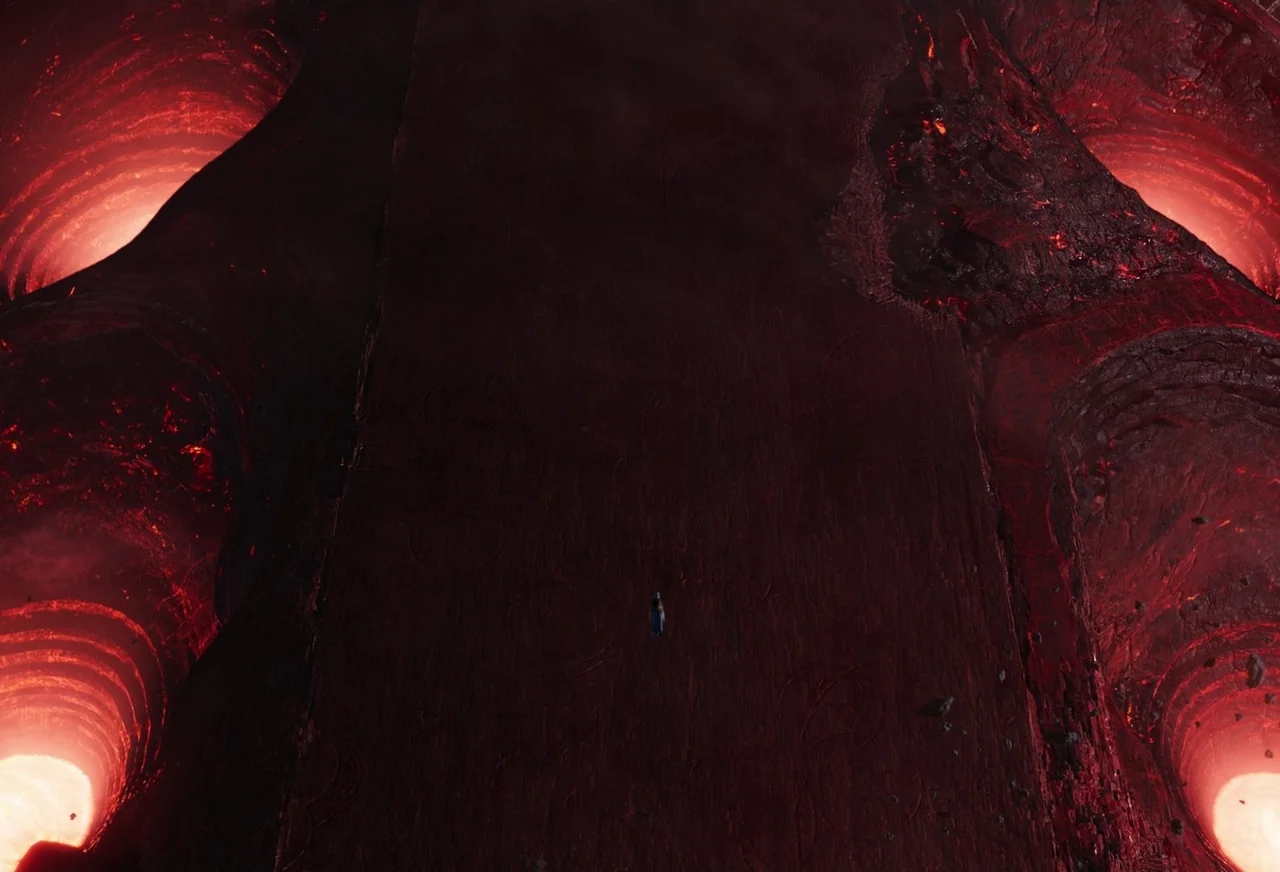 Eternals (2021) movie still: establishing — A dark, jagged volcanic plateau is surrounded by several deep, glowing molten lava pits. The landscape…