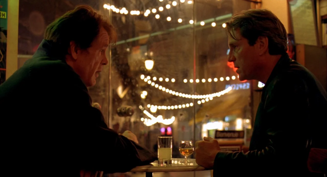 The Good Thief (2002) movie still: medium — A cafe booth at night with a glass window displaying blurred city lights. Two men sit opposite each…