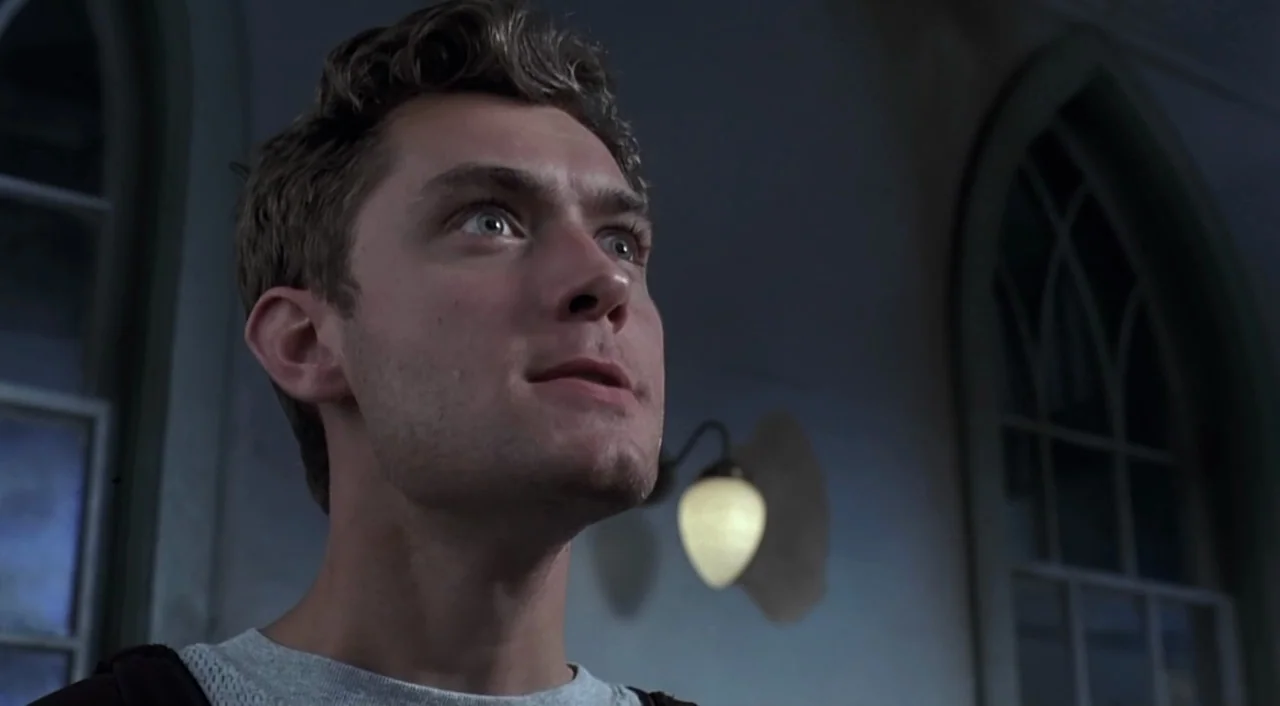 eXistenZ (1999) movie still: closeup — A dimly lit interior with arched windows and a wall-mounted glass lamp fixture. A young man stares upward…