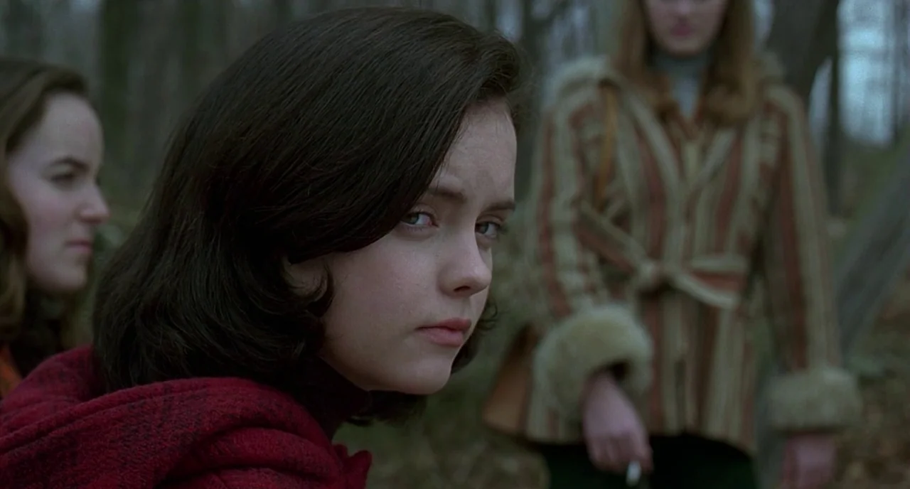 The Ice Storm (1997) movie still: medium — Three young women stand in a dense, overcast woodland area with bare, skeletal trees. One woman in a dark…