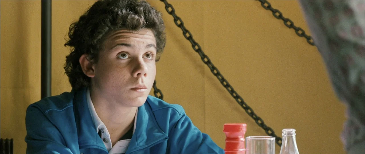 Rivals (1972) movie still: medium — A yellow-walled diner booth features a black chain hanging on the wall. A young man wearing a blue jacket gazes…