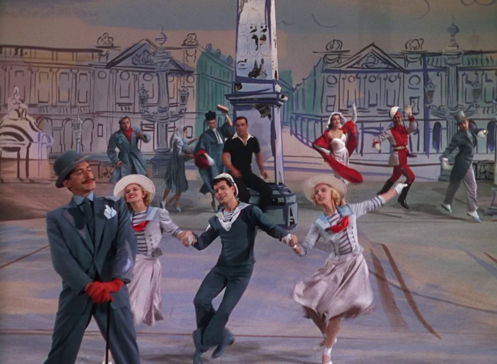 An American In Paris (1951) movie still: fullbody — A musical performance takes place on a stage featuring a painted backdrop of Paris. Dancers in…