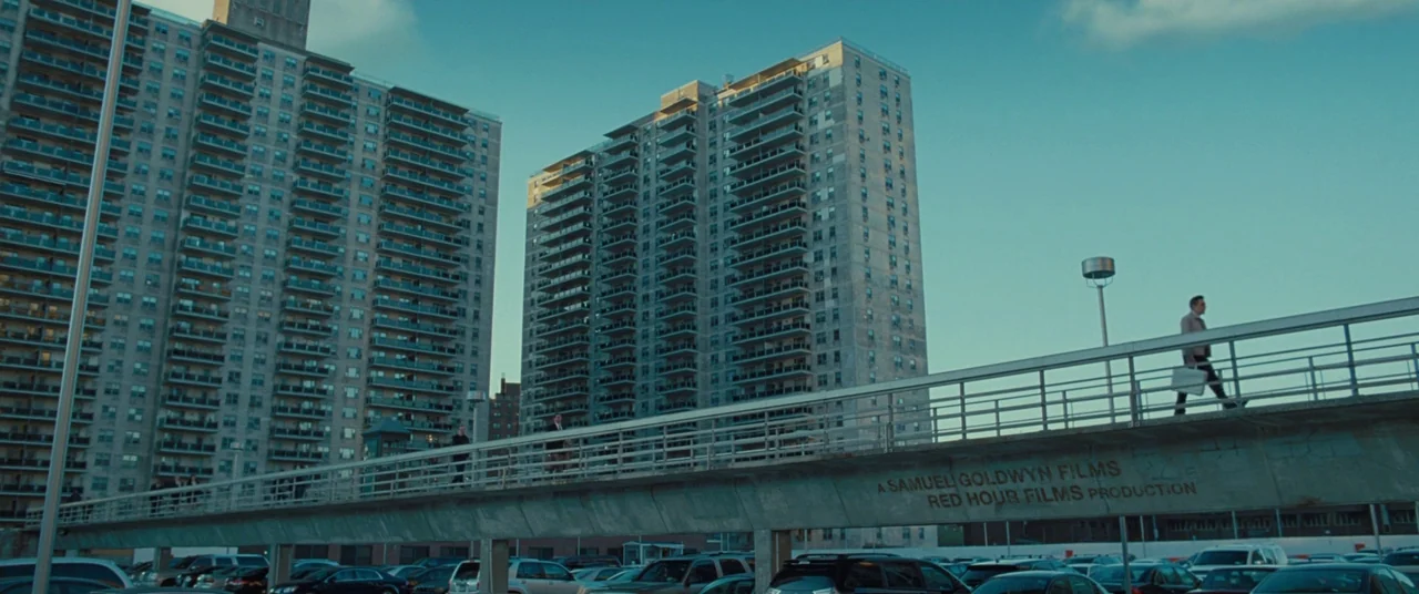 The Secret Life of Walter Mitty (2013) movie still: wide — A tall, industrial pedestrian bridge spans across a crowded parking lot beneath two large…