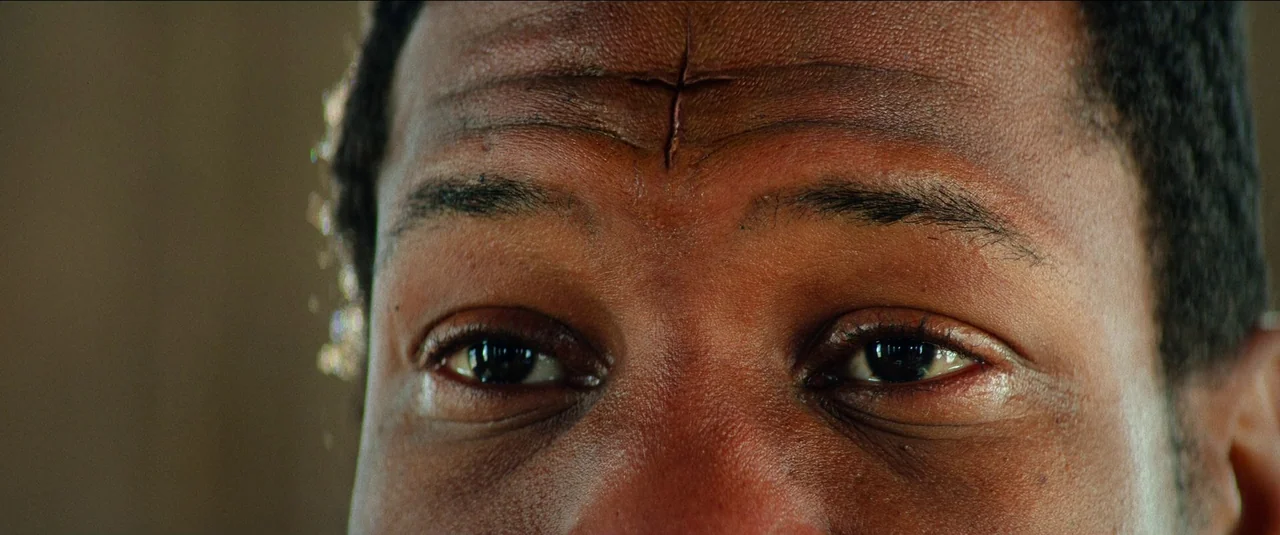 The Harder They Fall (2021) movie still: closeup — A close up on a man's forehead and eyes. A horizontal scar is prominently displayed on the…