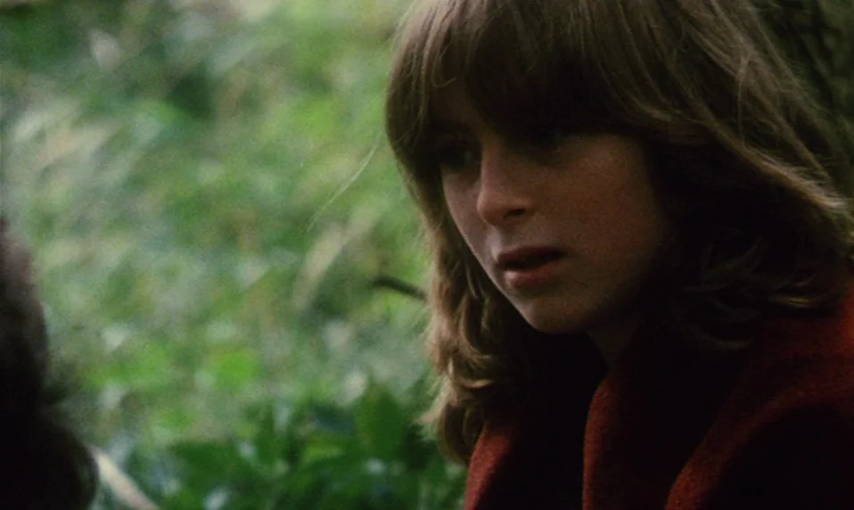 Black Jack (1979) movie still: closeup — A dense patch of out-of-focus green foliage fills the frame behind a young woman. The person has…