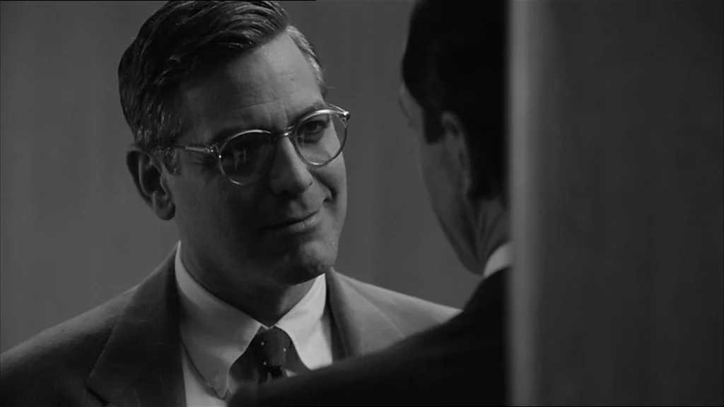 Good Night And Good Luck (2005) movie still: closeup — A dimly lit room provides the backdrop for a conversation between two men. One man in glasses…