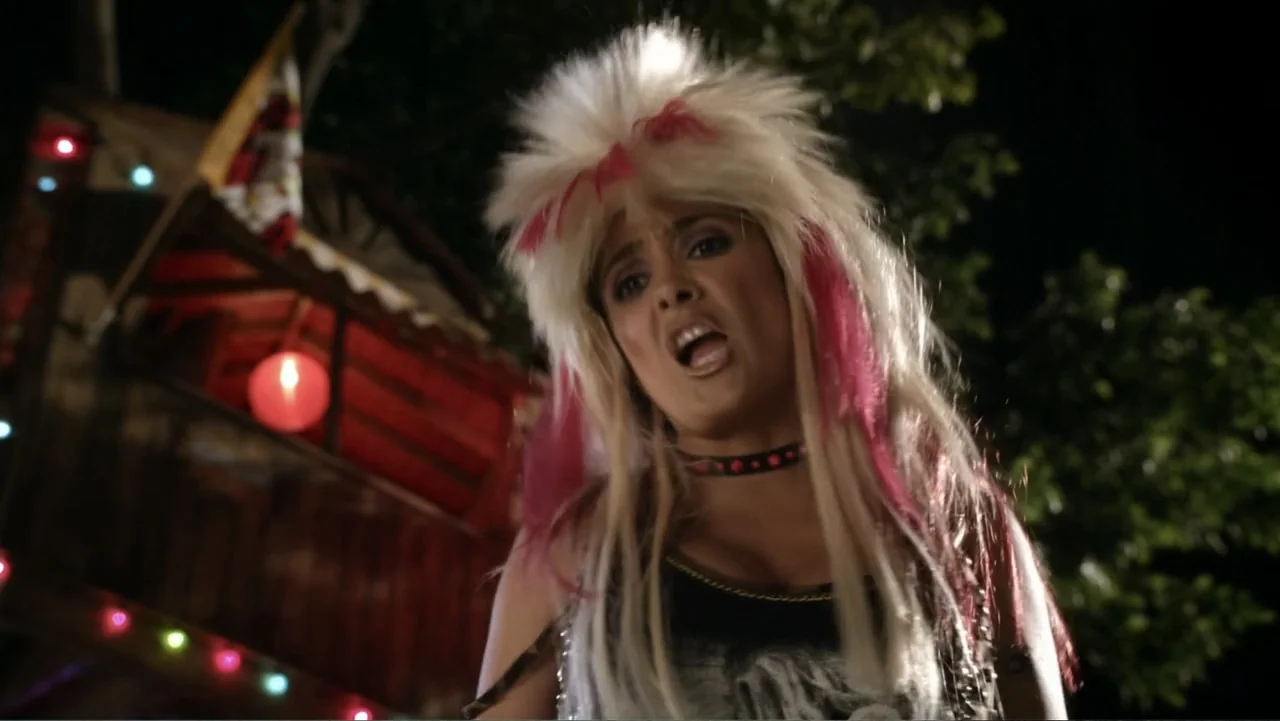 Grown Ups 2 (2013) movie still: medium — A nighttime backyard setting features a woman in front of a blurred wooden structure. The woman wears 1980s…