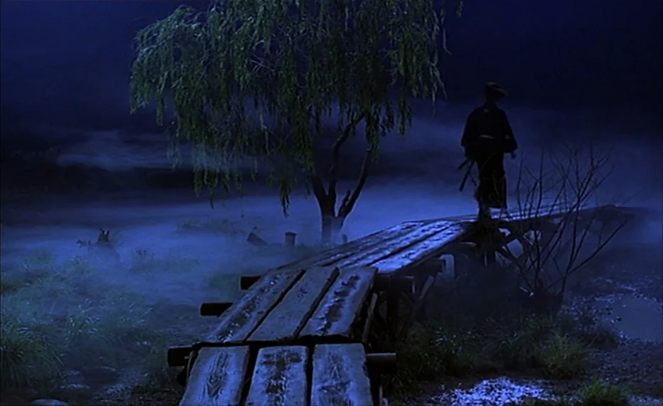 Gohatto (1999) movie still: wide — A night landscape features a narrow wooden footbridge crossing over a fog-filled area. A lone figure in…
