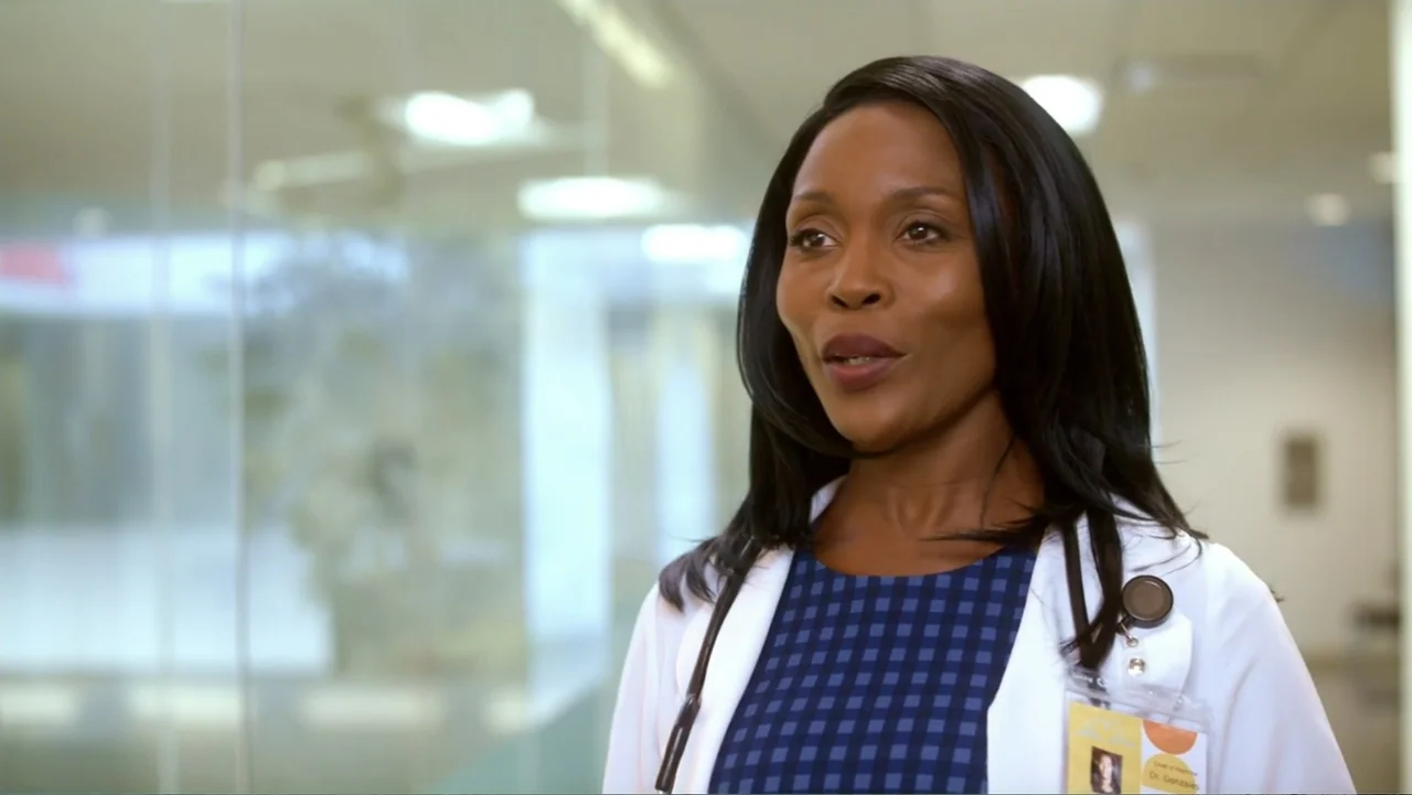 Christmas with a Prince (2018) movie still: medium — A modern hospital corridor with glass walls and bright sterile lighting. A female doctor in a…